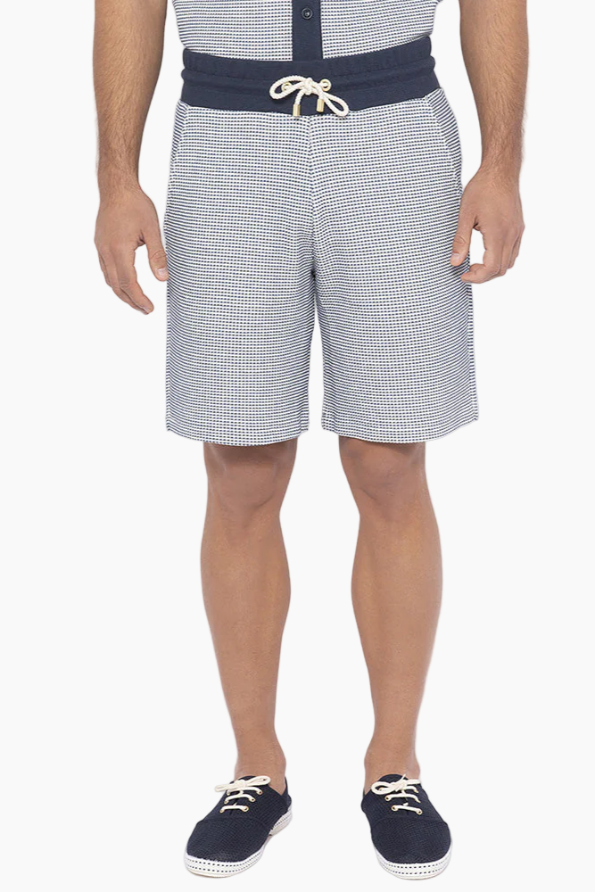 A man wearing a blue collared shirt and blue shorts and navy shoes
