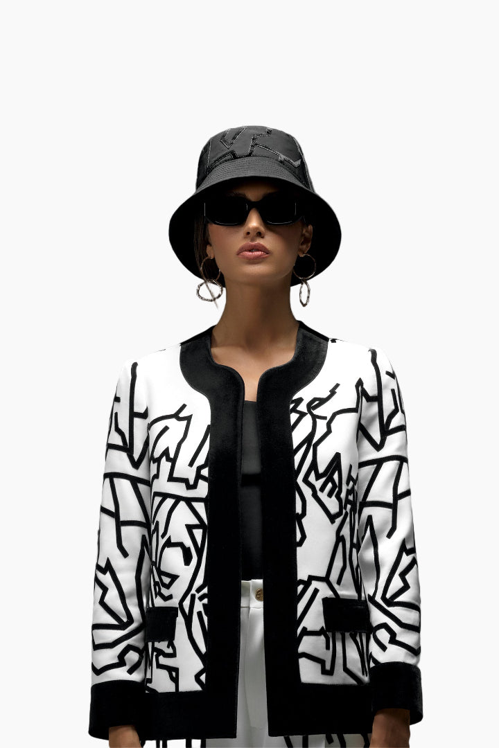 Person wearing a black and white patterned jacket with a black hat and sunglasses on a white background