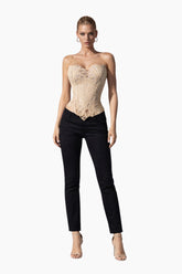 Woman wearing a beige lace corset top and black pants on a white background