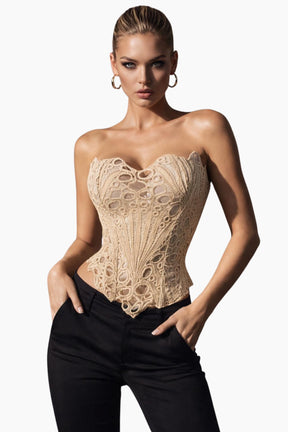 Woman wearing a beige lace corset and black pants on a white background