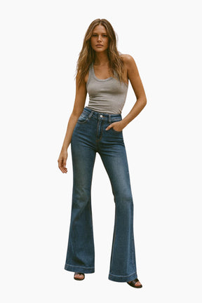 Woman wearing a beige tank top and blue flared jeans on a white background