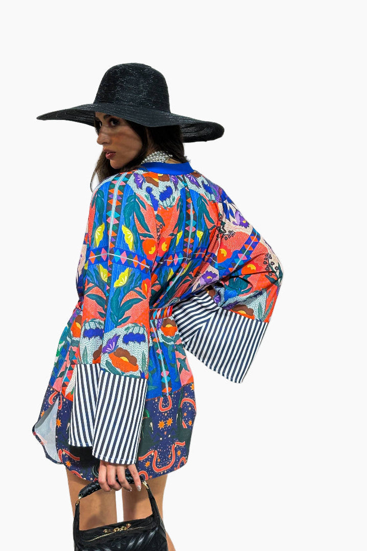 Woman wearing a colorful kimono-style garment with a black hat on a white background