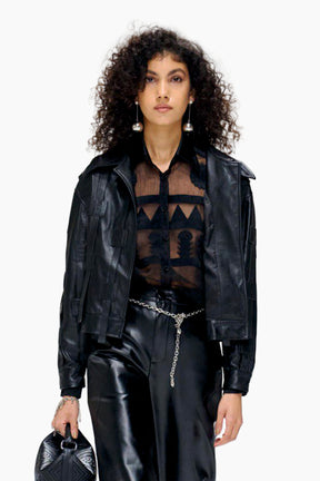 Person wearing a black leather jacket and pants with a sheer top, holding a black handbag.