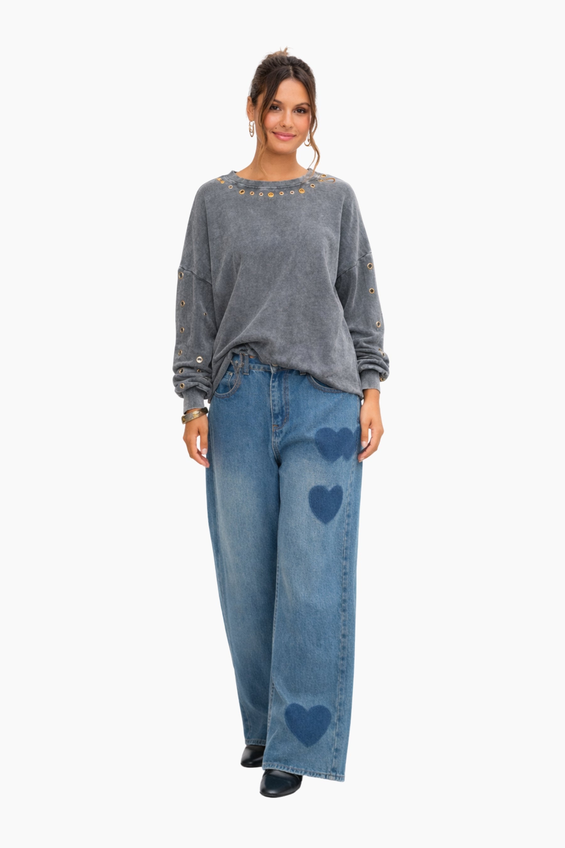 Woman wearing a gray sweatshirt and blue jeans with heart designs on a white background