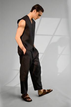 Man wearing a black sleeveless top and pants against a green screen.