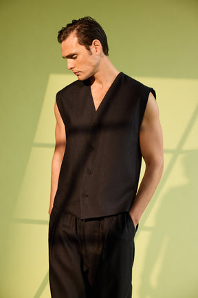 Man wearing a black sleeveless top and pants against a green background