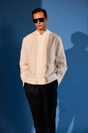 Man wearing a light-colored jacket and dark pants against a blue background