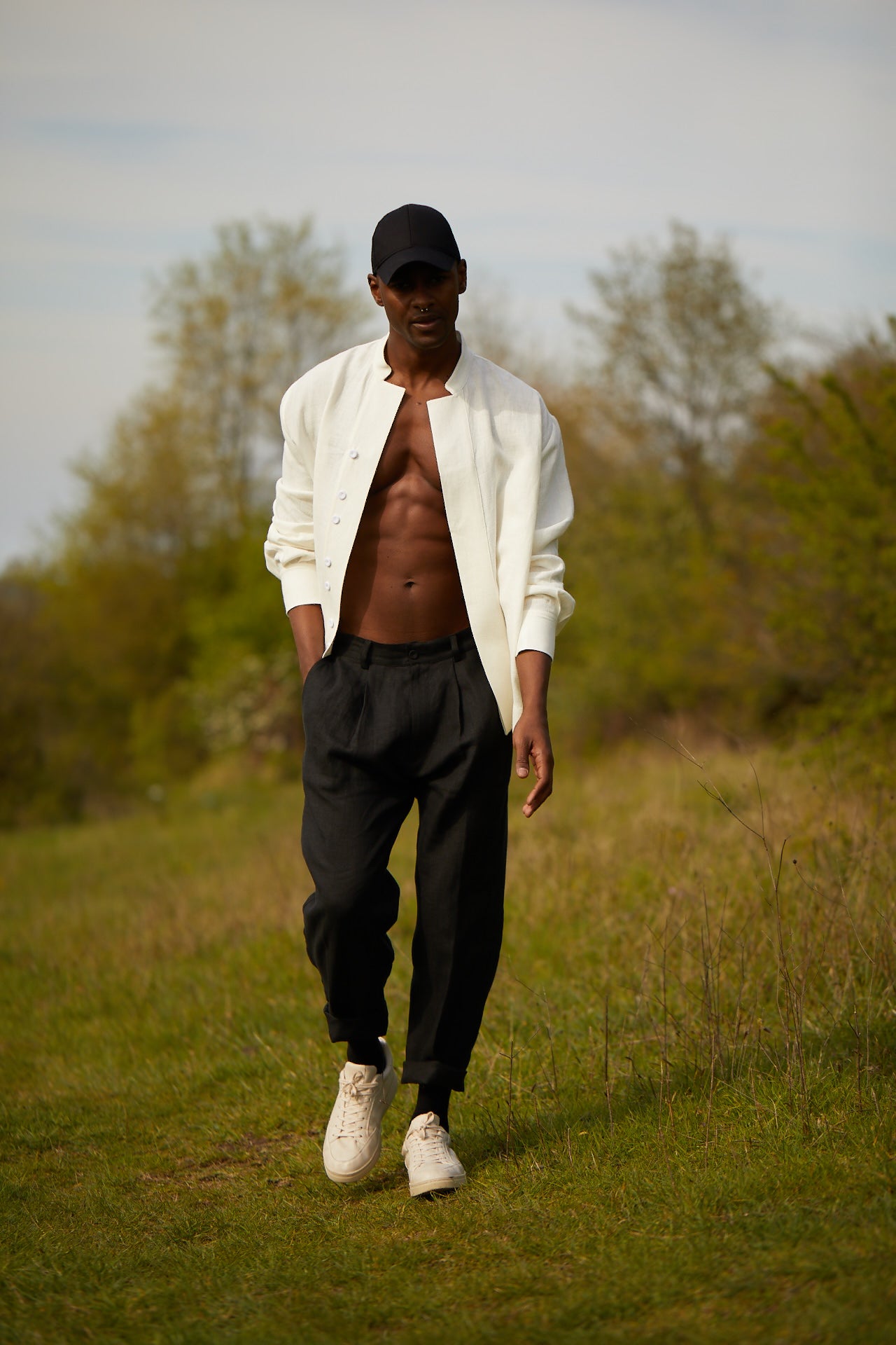 Man walking in a field wearing a white shirt, black pants, and white sneakers.