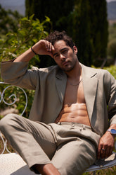 Man in beige suit sitting outdoors with greenery in the background