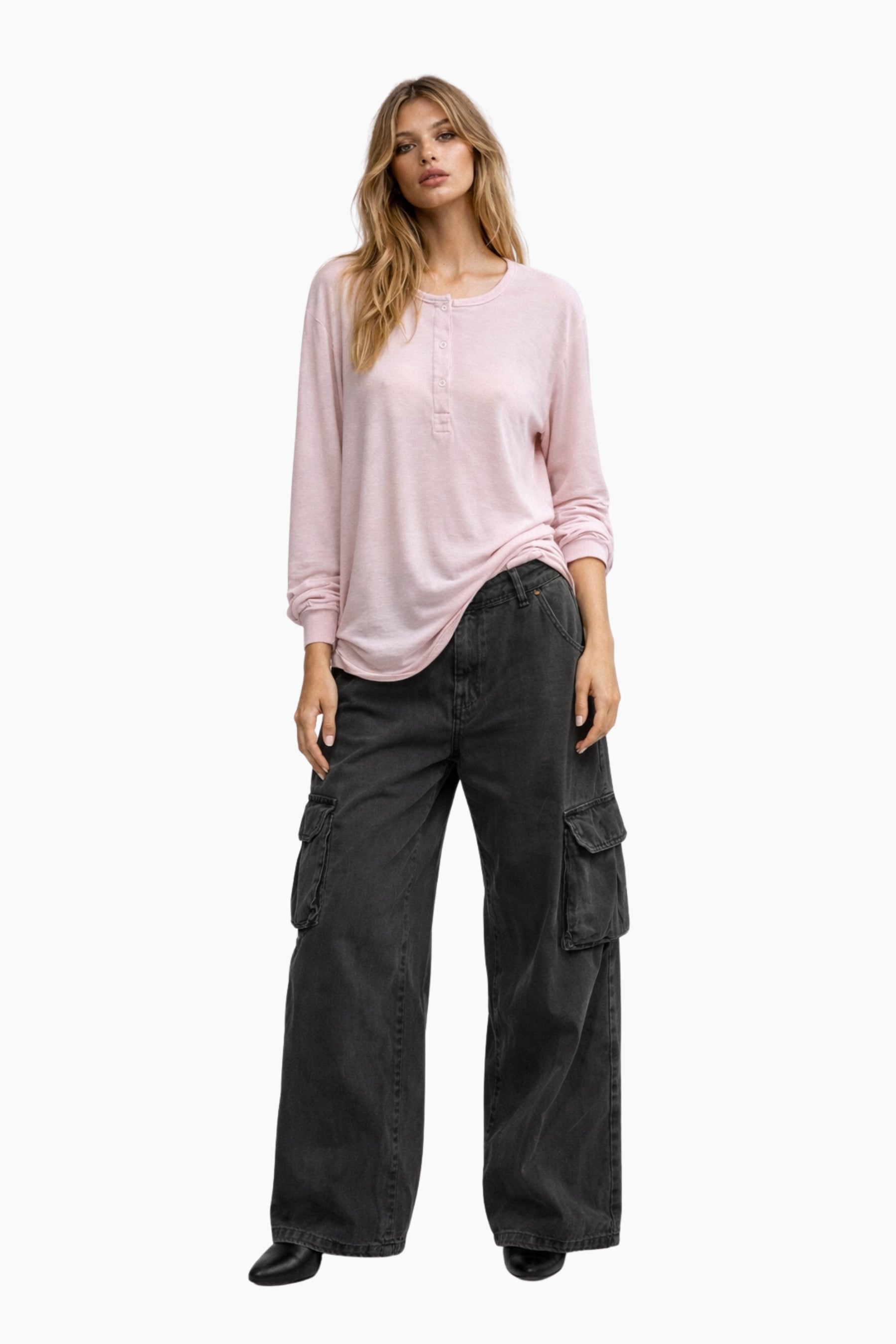 Woman wearing a pink long-sleeve top and black cargo pants on a white background
