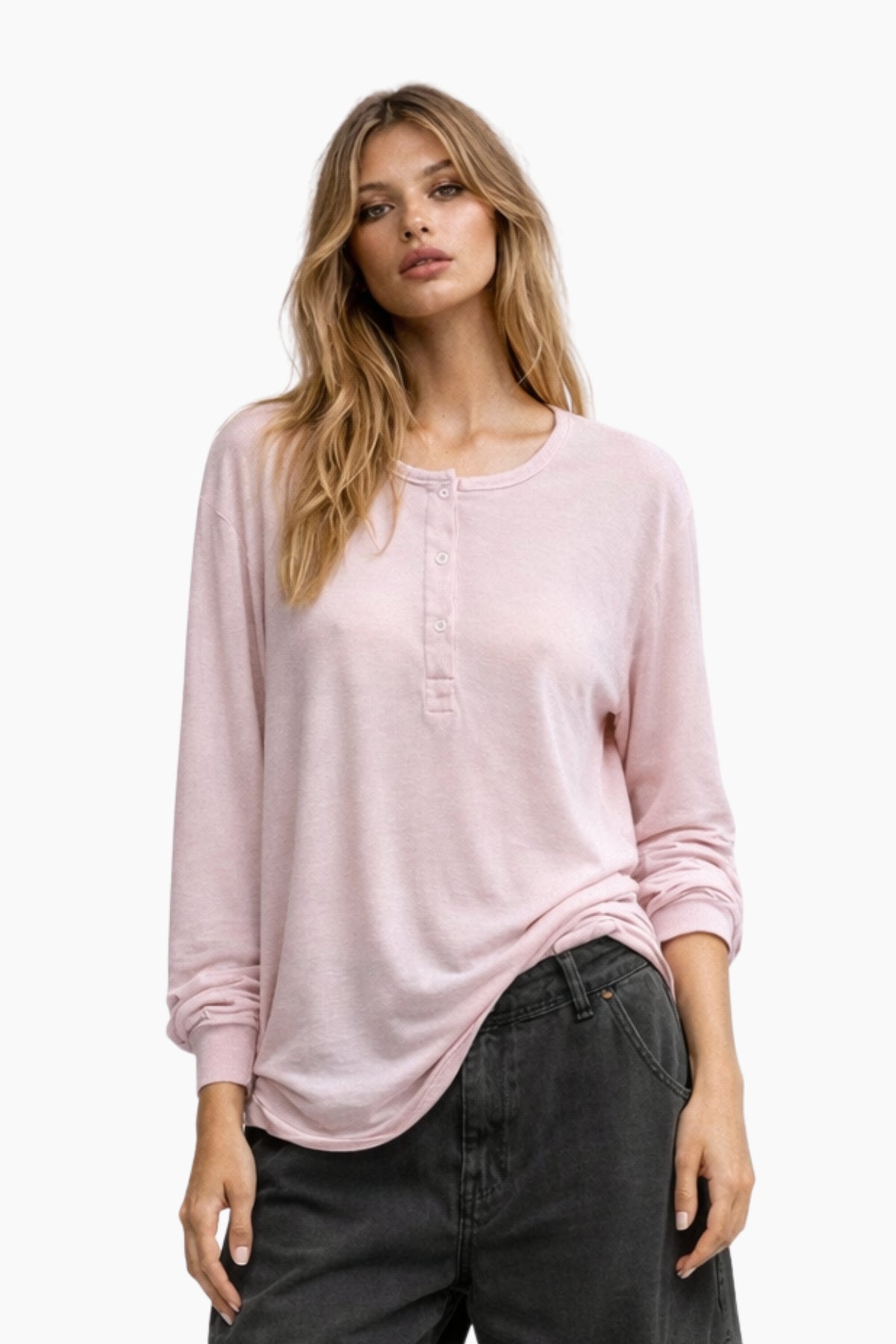 Woman wearing a light pink long-sleeve top and dark jeans on a white background