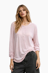 Woman wearing a light pink long-sleeve top and dark jeans on a white background