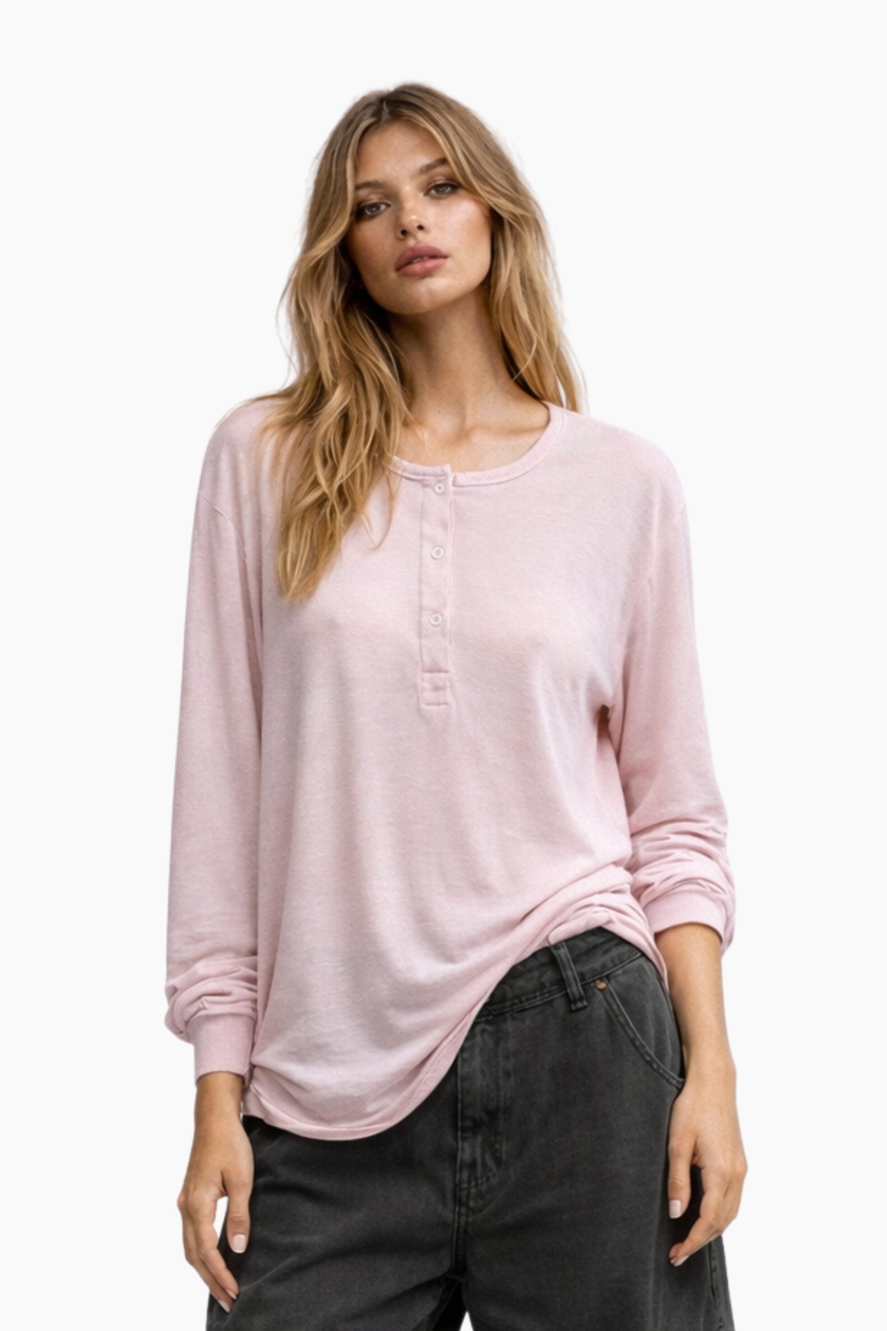 Woman wearing a light pink long-sleeve top and dark jeans on a white background