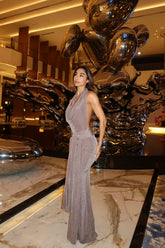 Woman in a gray dress standing in front of a large metallic sculpture in an indoor setting.