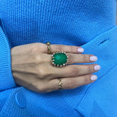 Hand wearing a green ring with a blue sweater background