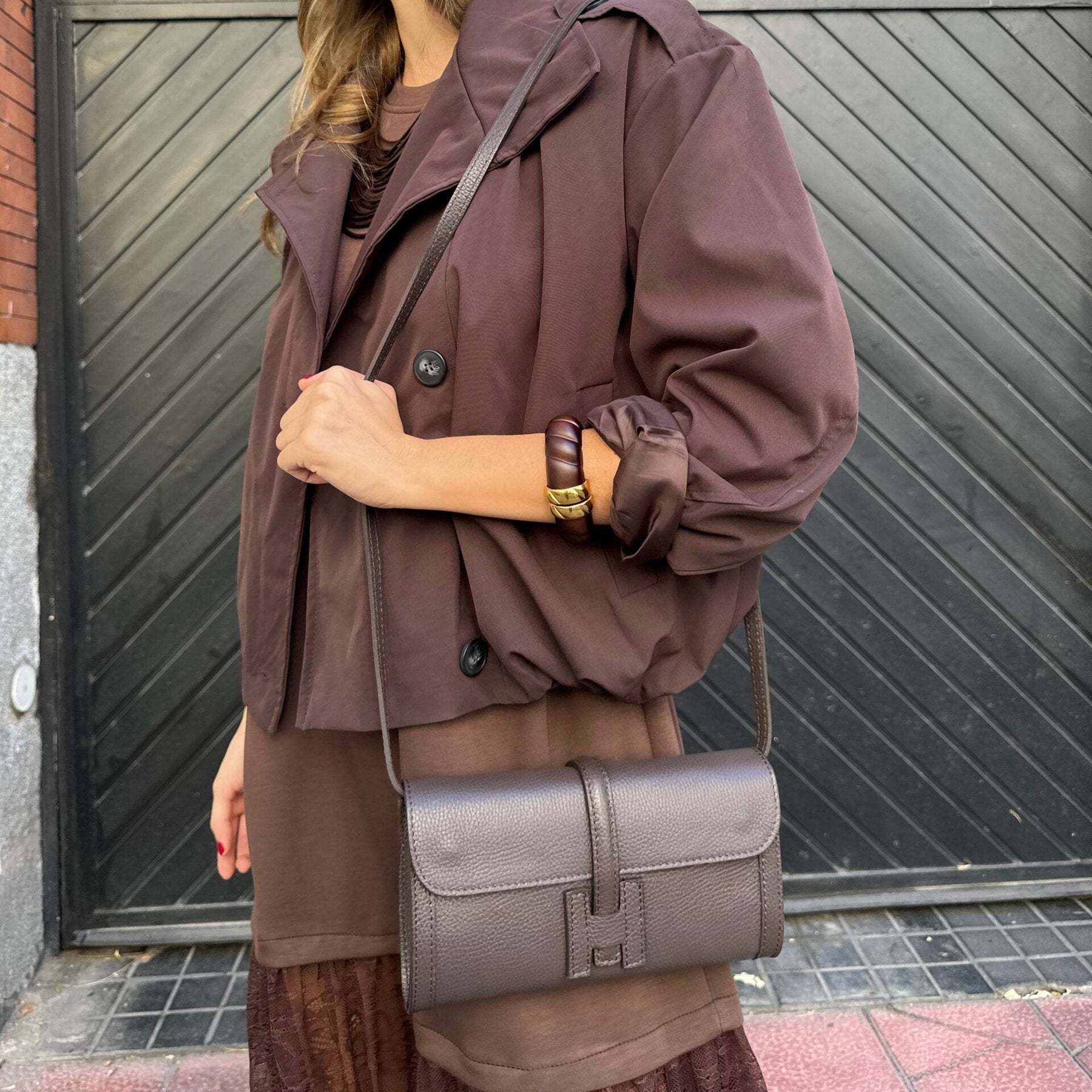 Woman in a brown coat with a gray bag standing 