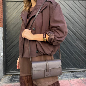 Woman in a brown coat with a gray bag standing 
