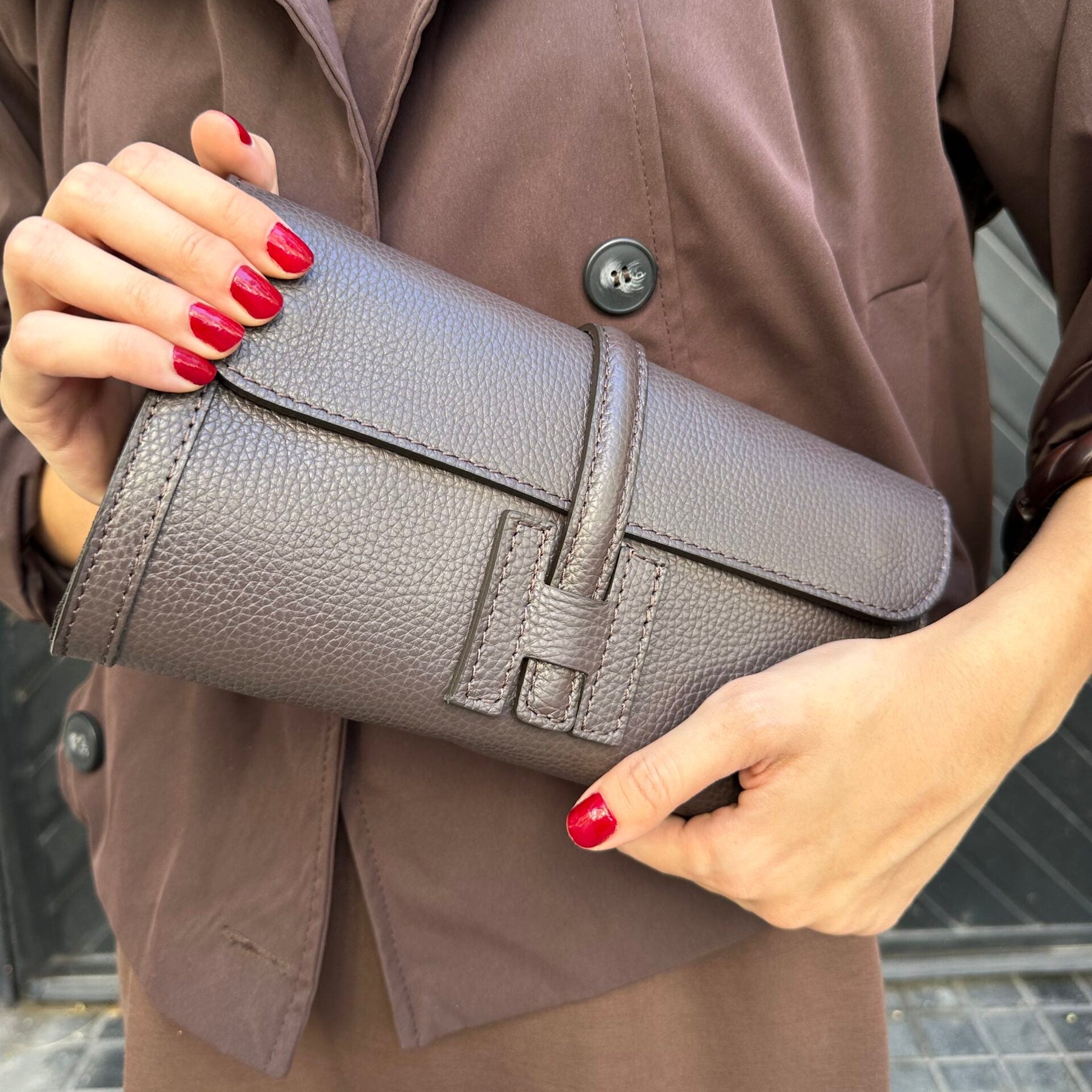Person holding a gray clutch with a brown coat