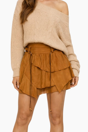 Person wearing a beige off-shoulder sweater and layered suede skirt on a white background
