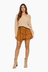 Woman wearing a beige off-shoulder top and brown suede skirt on a white background