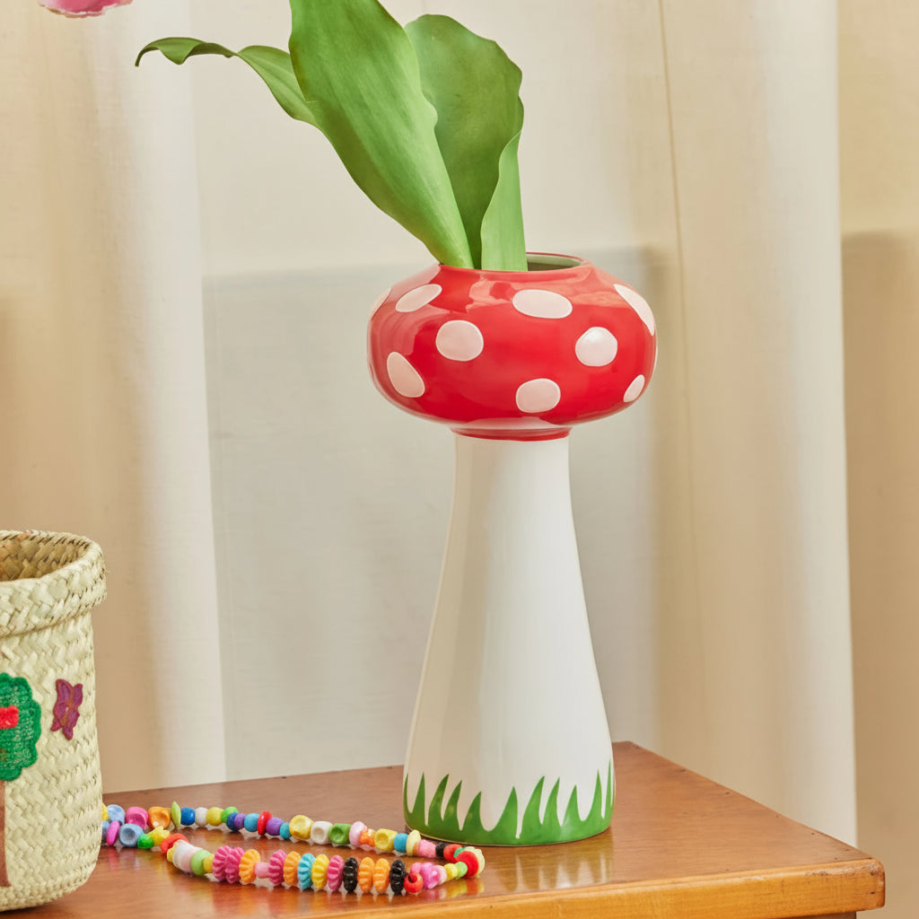 Decorative vase with red top and white polka dots on a wooden table with a pink flower.
