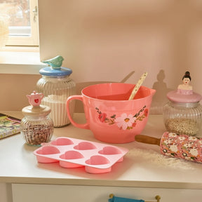 Pink kitchen items including a mixing bowl, baking tray, and rolling pin on a countertop.