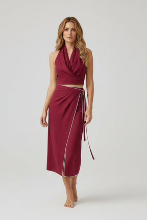 Woman wearing a burgundy dress with a halter top and wrap skirt on a white background