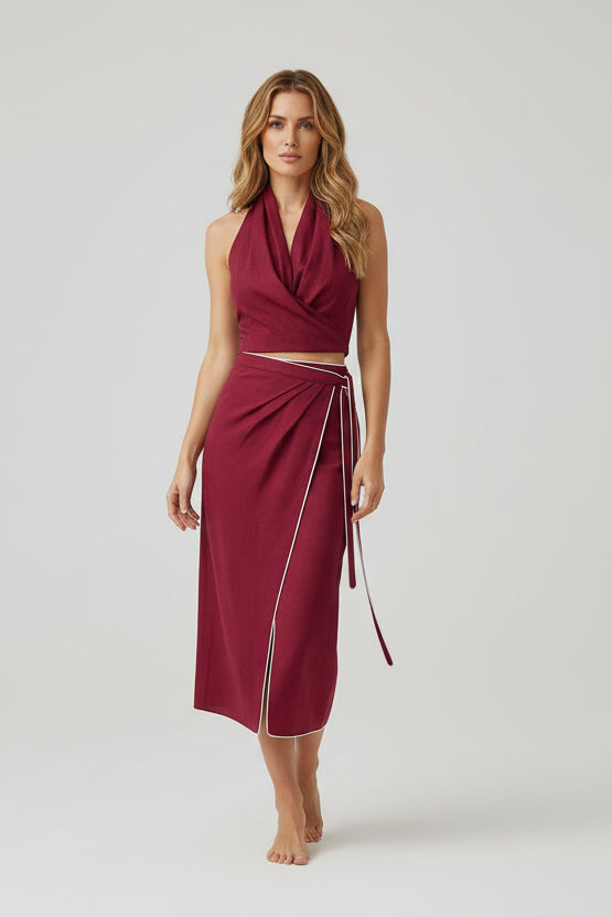 Woman wearing a burgundy dress with a halter top and wrap skirt on a white background