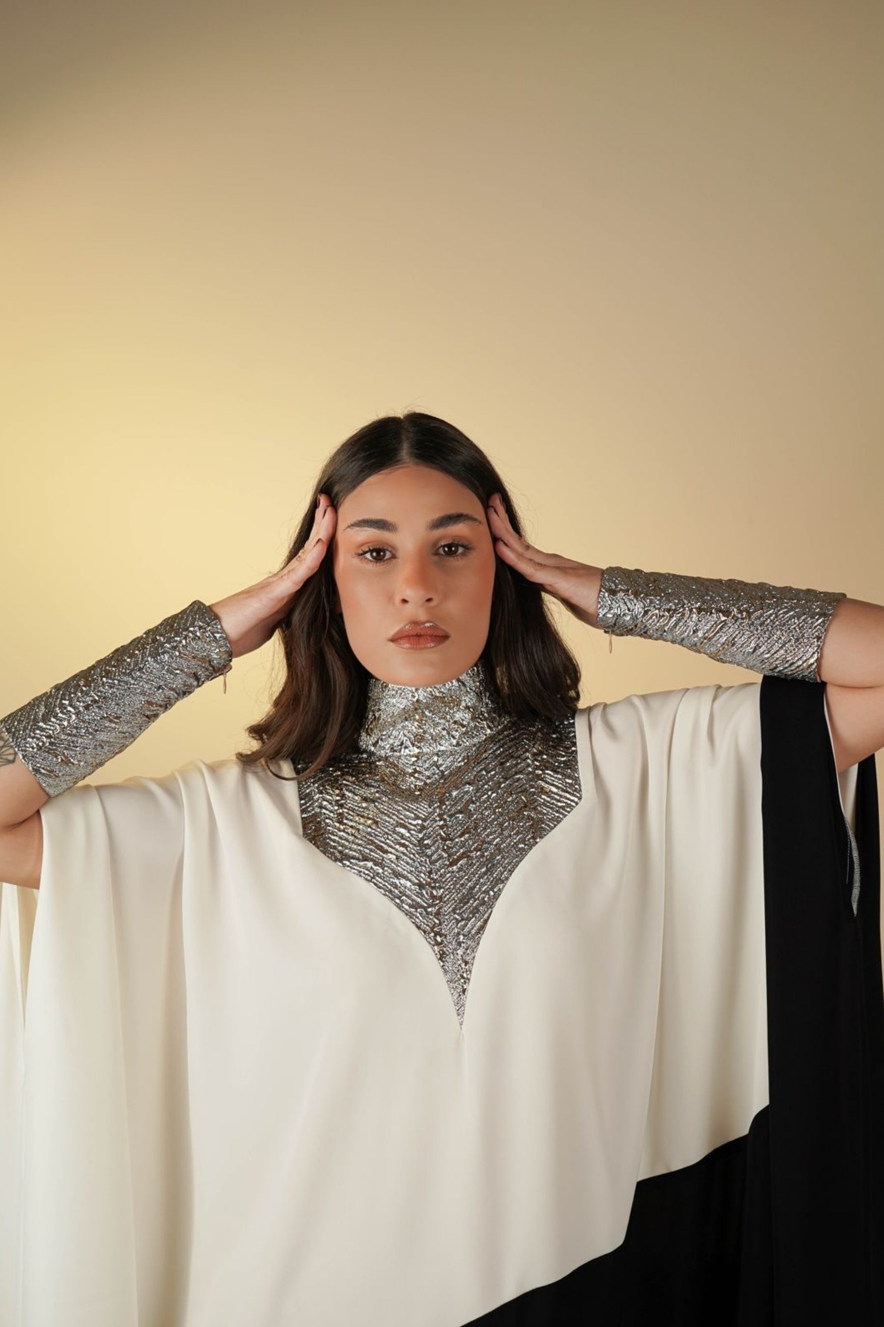 Woman wearing a silver chainmail shirt and white cape against a beige background
