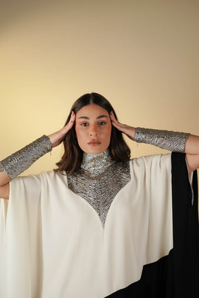 Woman wearing a silver chainmail shirt and white cape against a beige background