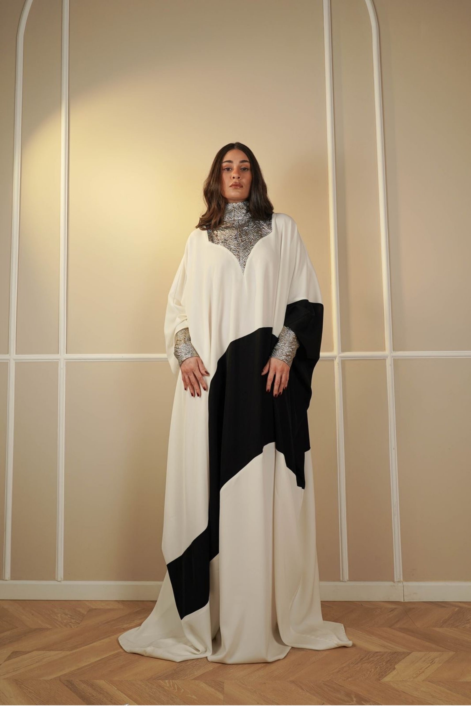Woman wearing a white and black dress with a patterned shawl against a neutral wall.
