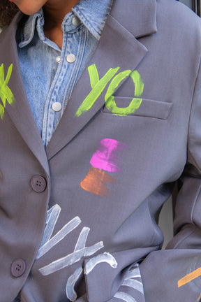 Gray blazer with colorful text and designs on a person wearing a denim shirt.