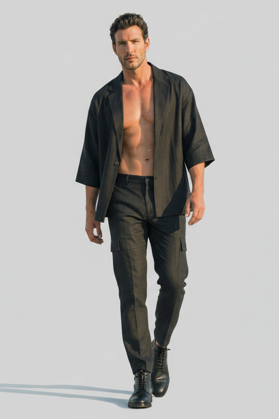 Man wearing a dark shirt over a tank top with dark pants on a light gray background