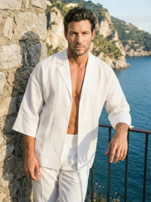 Man in a white outfit standing by a stone wall with a scenic ocean view.