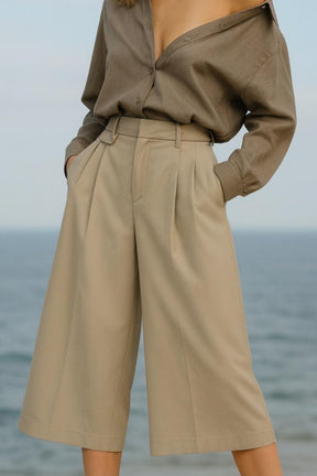 Person wearing a beige outfit with wide-leg pants and a matching top against a blurred ocean background