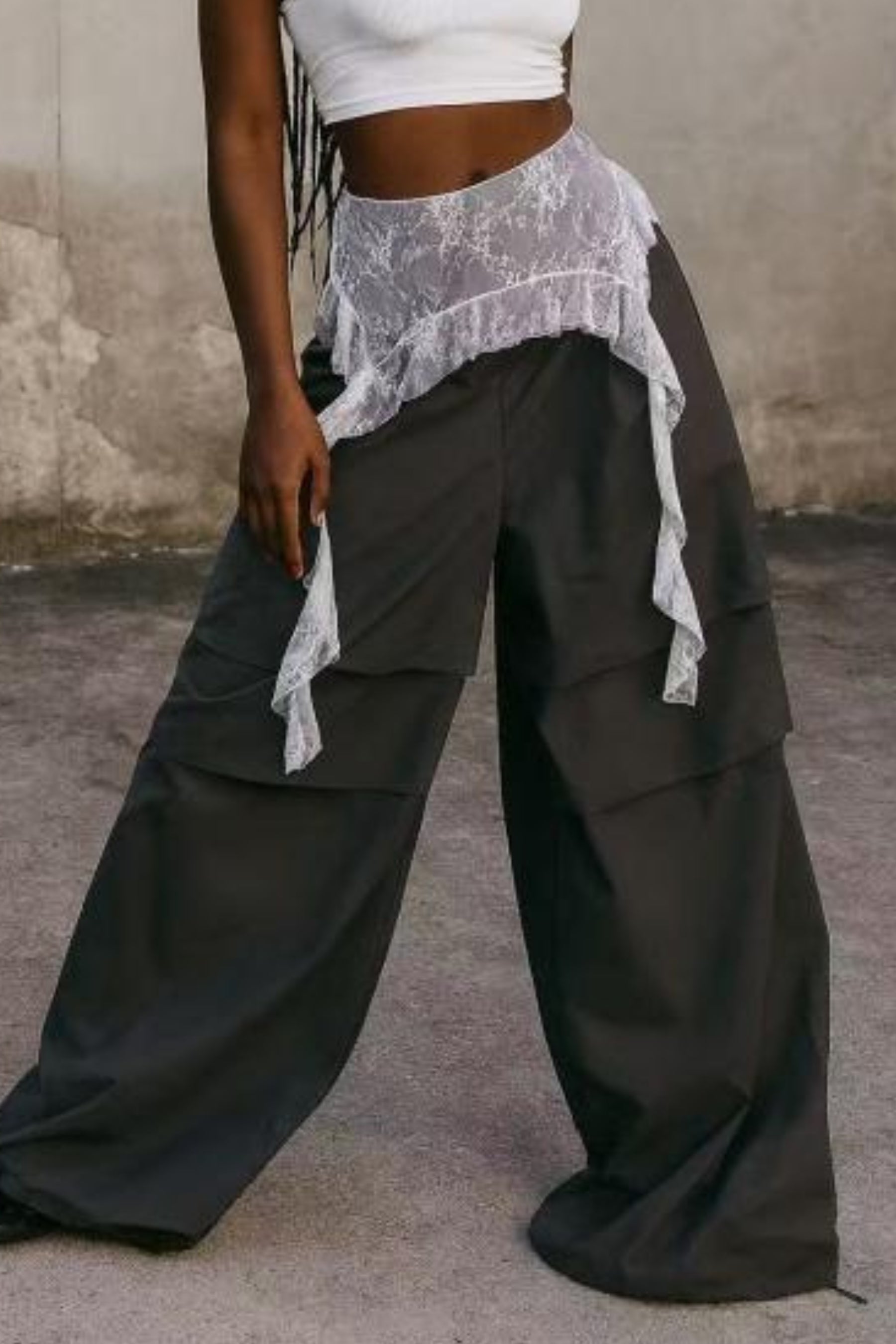 Person wearing wide-leg black pants with a white top and sheer overlay against a neutral background