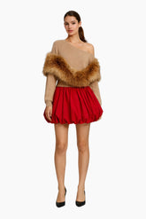 Woman wearing a beige off-shoulder top with fur trim and a red skirt on a white background