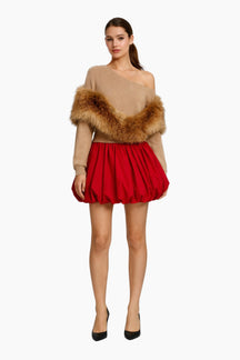 Woman wearing a beige off-shoulder top with fur trim and a red skirt on a white background