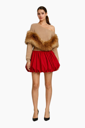 Woman wearing a beige off-shoulder top with fur trim and a red skirt on a white background
