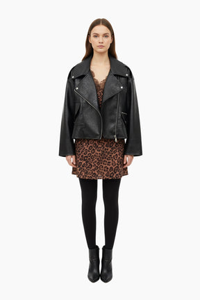 Woman wearing a black leather jacket, leopard print skirt, and black tights 