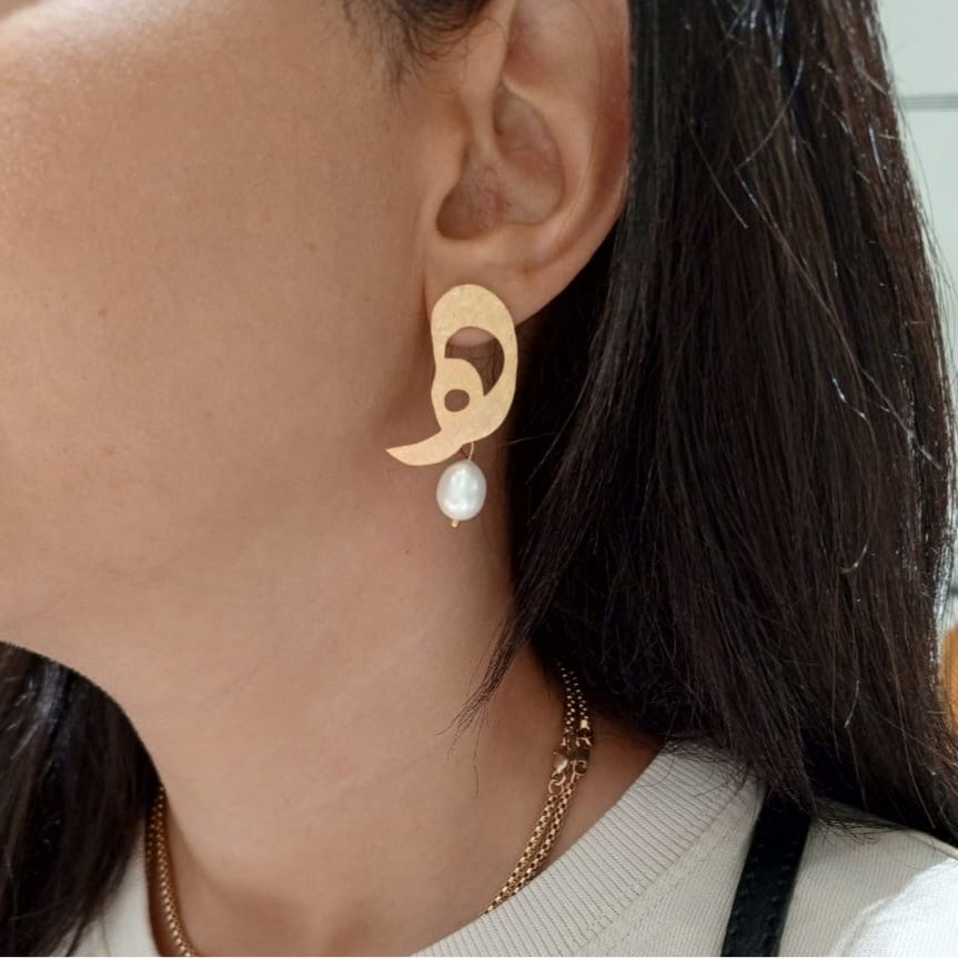 Close-up of a person wearing a gold earring with a pearl drop.