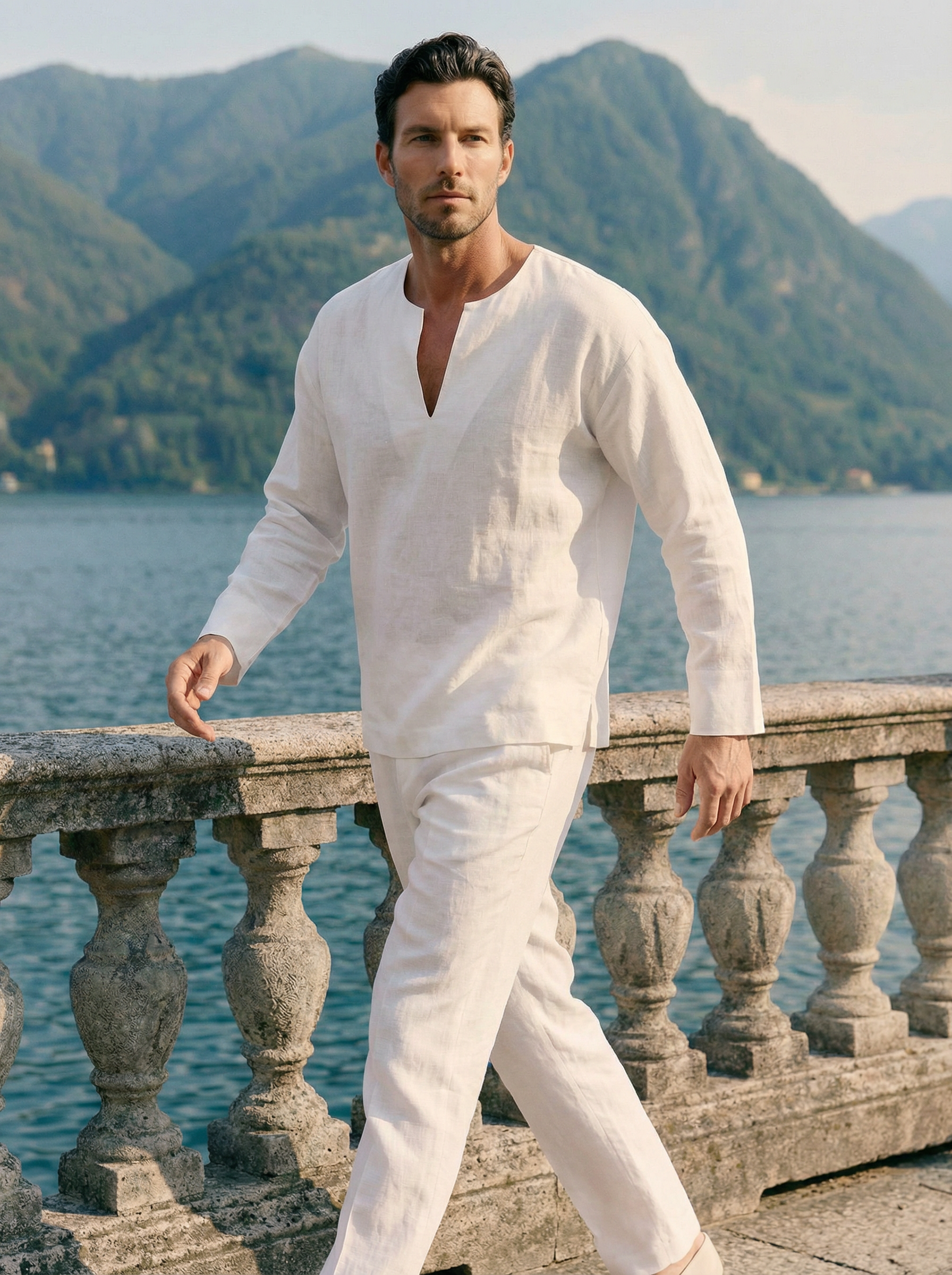 Man in a white outfit standing by a scenic lakeside with mountains in the background