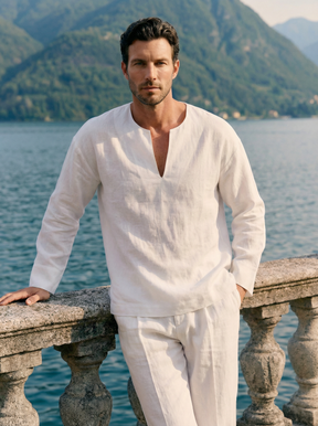 Man in a white outfit standing by a scenic lakeside with mountains in the background