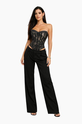 Woman wearing a black lace strapless top and high-waisted black pants on a white background