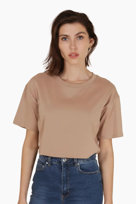 Woman wearing a beige t-shirt and blue jeans against a beige background