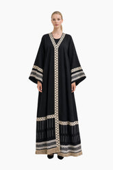 Woman wearing a black abaya with white embroidery on a white background