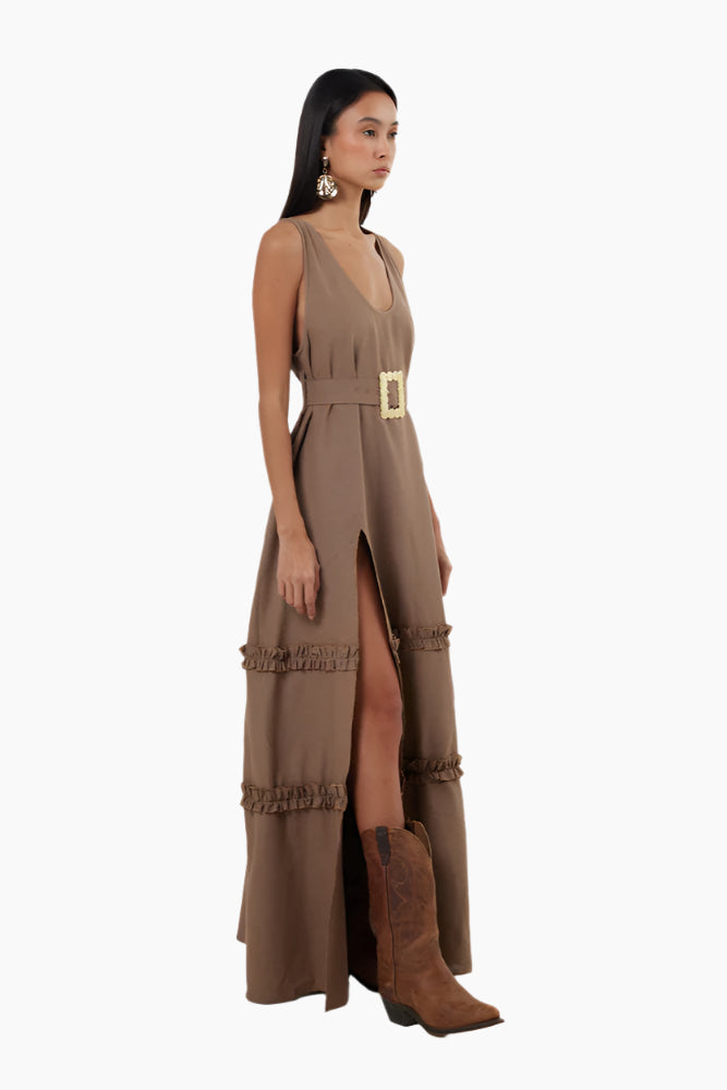 Woman wearing a brown dress with a belt . Floor-length dress with double ruffles, deep rounded neckline, belt, and a slit.