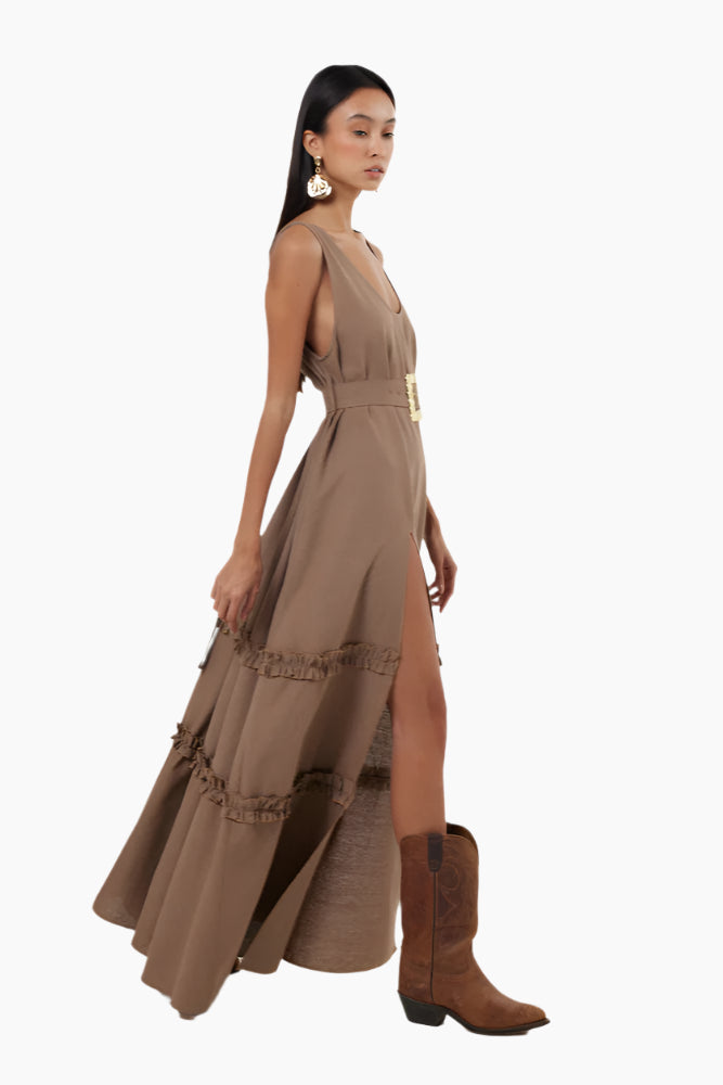 Woman wearing a brown dress with a belt . Floor-length dress with double ruffles, deep rounded neckline, belt, and a slit.