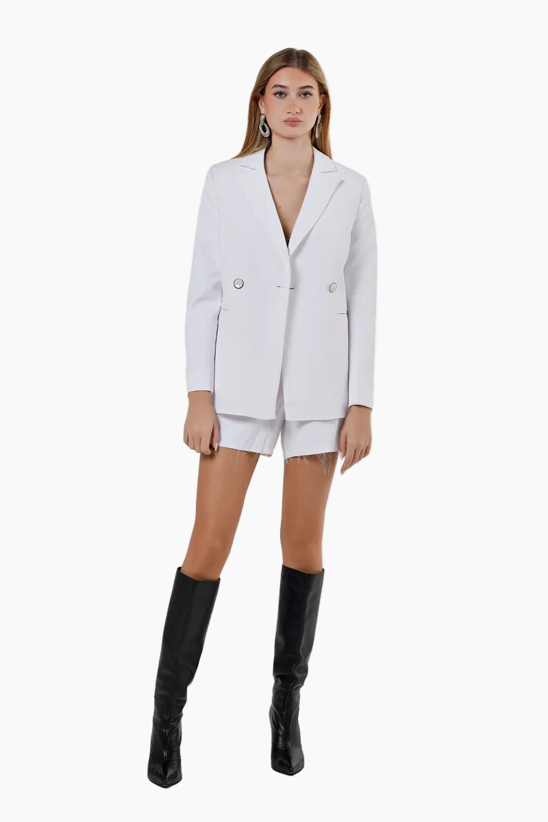 Woman wearing a white blazer and black knee-high boots on a white background