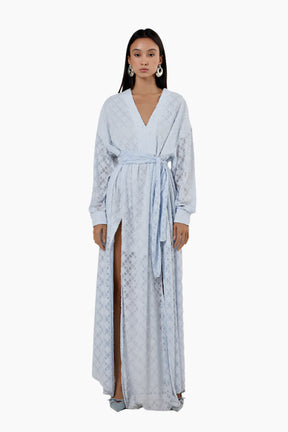 Woman wearing a light blue patterned dress with a slit. Flared floor-length dress with a V-neckline, balloon sleeves, two side slits, and a waist belt.